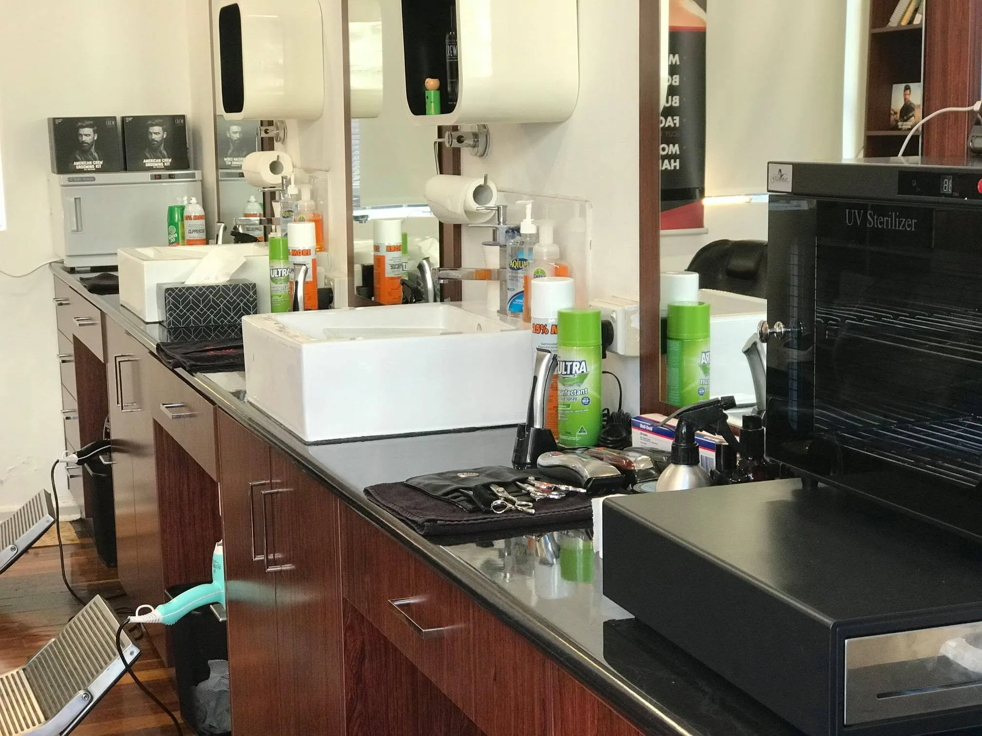Barber station interior — twin vessel sinks, product shelves, dark timber cabinetry